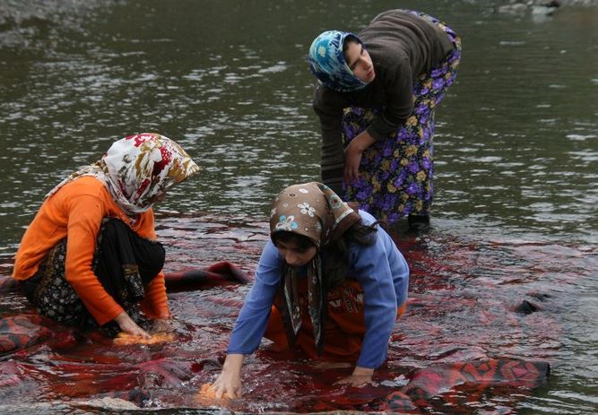 Iranian women washing a hand-woven carpet in a lake.